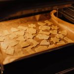 Ausgestochene Plätzchen aus Teig auf Backpapier werden in den Ofen geschoben