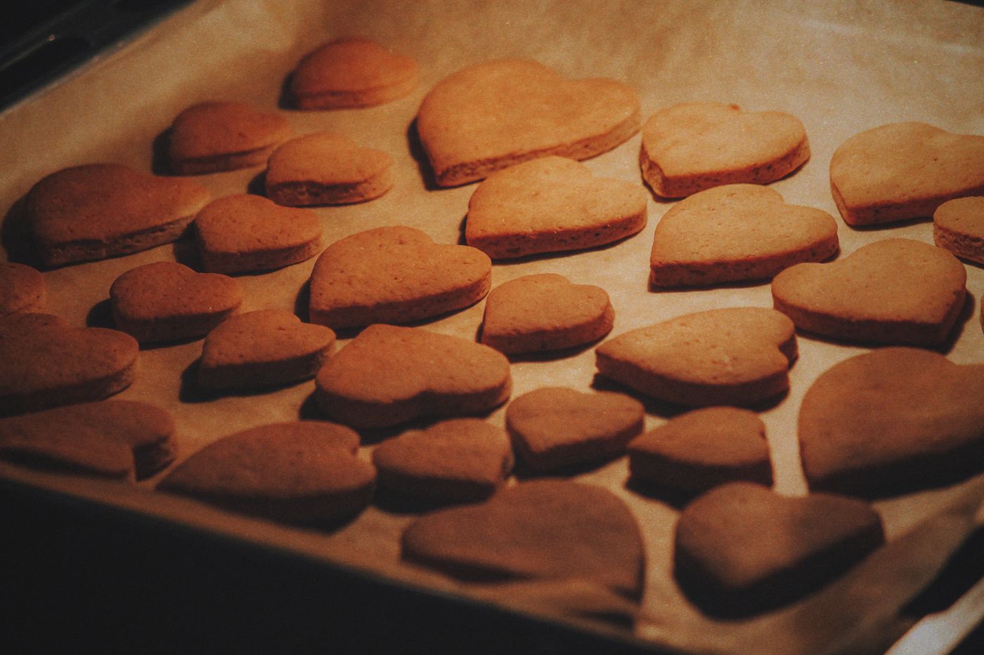 Rows of heart-shaped biscuits on a baking tray lined with parchment