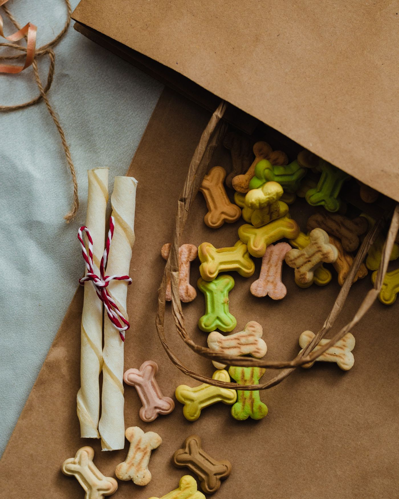 Colorful bone-shaped dog treats spilling from a kraft paper bag